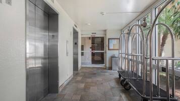 A hallway with elevators, a trash bin, and a security camera.