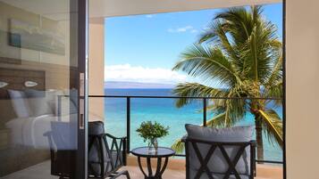 A balcony with a view of the ocean, two chairs, a small table, and a plant.