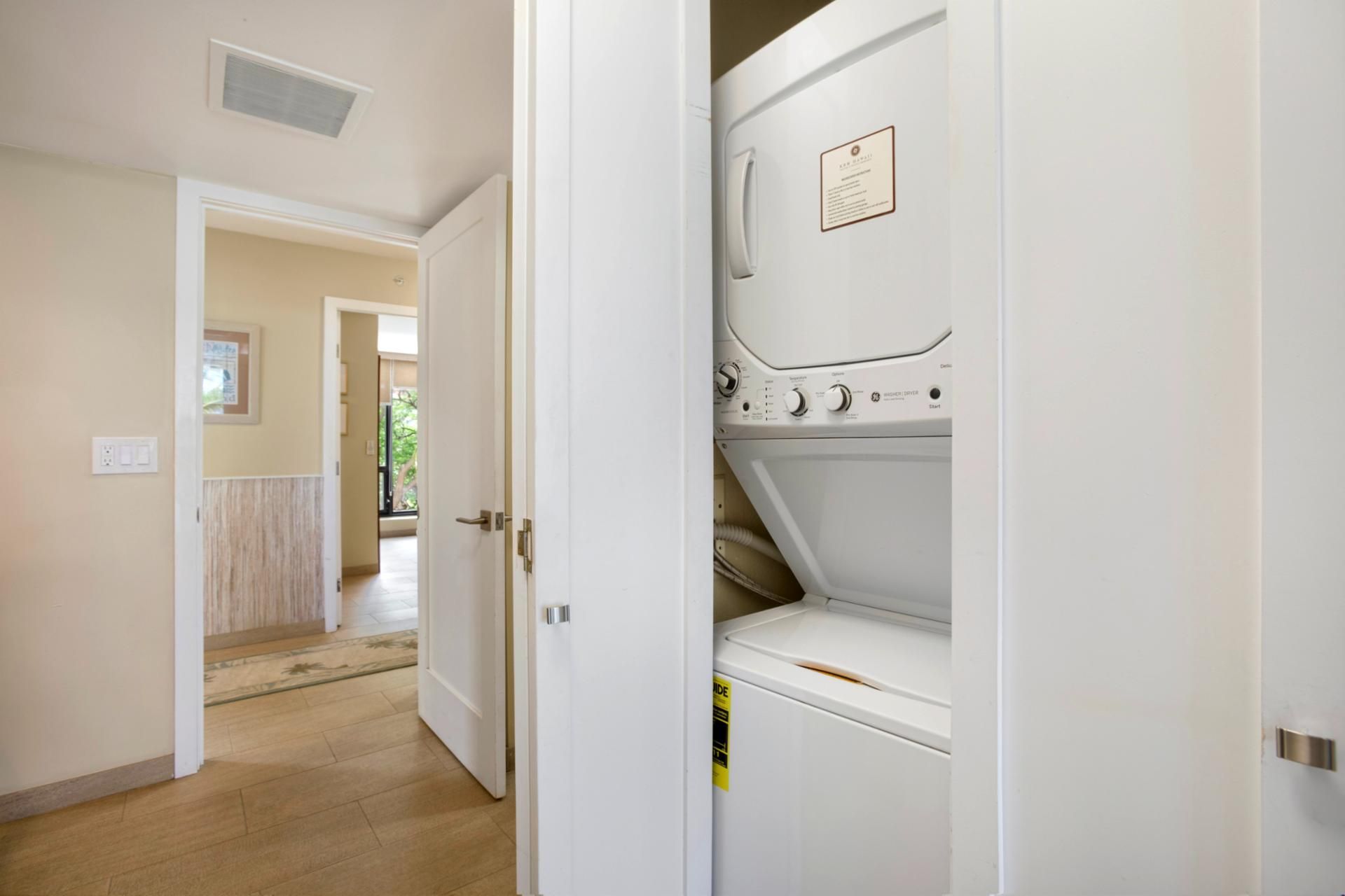 Une buanderie équipée d’un lave-linge et d’un sèche-linge à chargement frontal, d’une porte donnant sur un couloir et d’une prise électrique visible sur le mur.