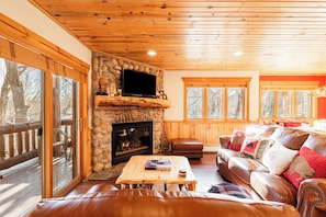 Un intérieur de chalet chaleureux avec une cheminée en pierre, des meubles en cuir et de grandes fenêtres.
