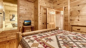 Quarto de cabana de madeira com uma cama, uma televisão sobre uma mesinha e um cartaz na parede.