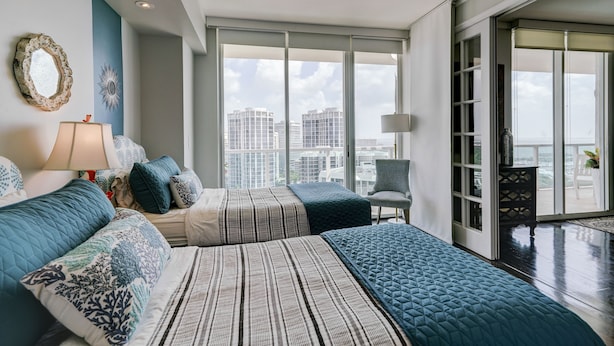 A modern bedroom with a large bed, a chair, and a view of the city through large windows. - Luxury Penthouse w/Private Rooftop Terrace in Coconut Grove Hotel! (Miami)
