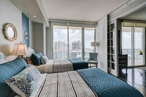 Une chambre moderne avec un grand lit, un fauteuil et une vue sur la ville grâce à de grandes fenêtres.