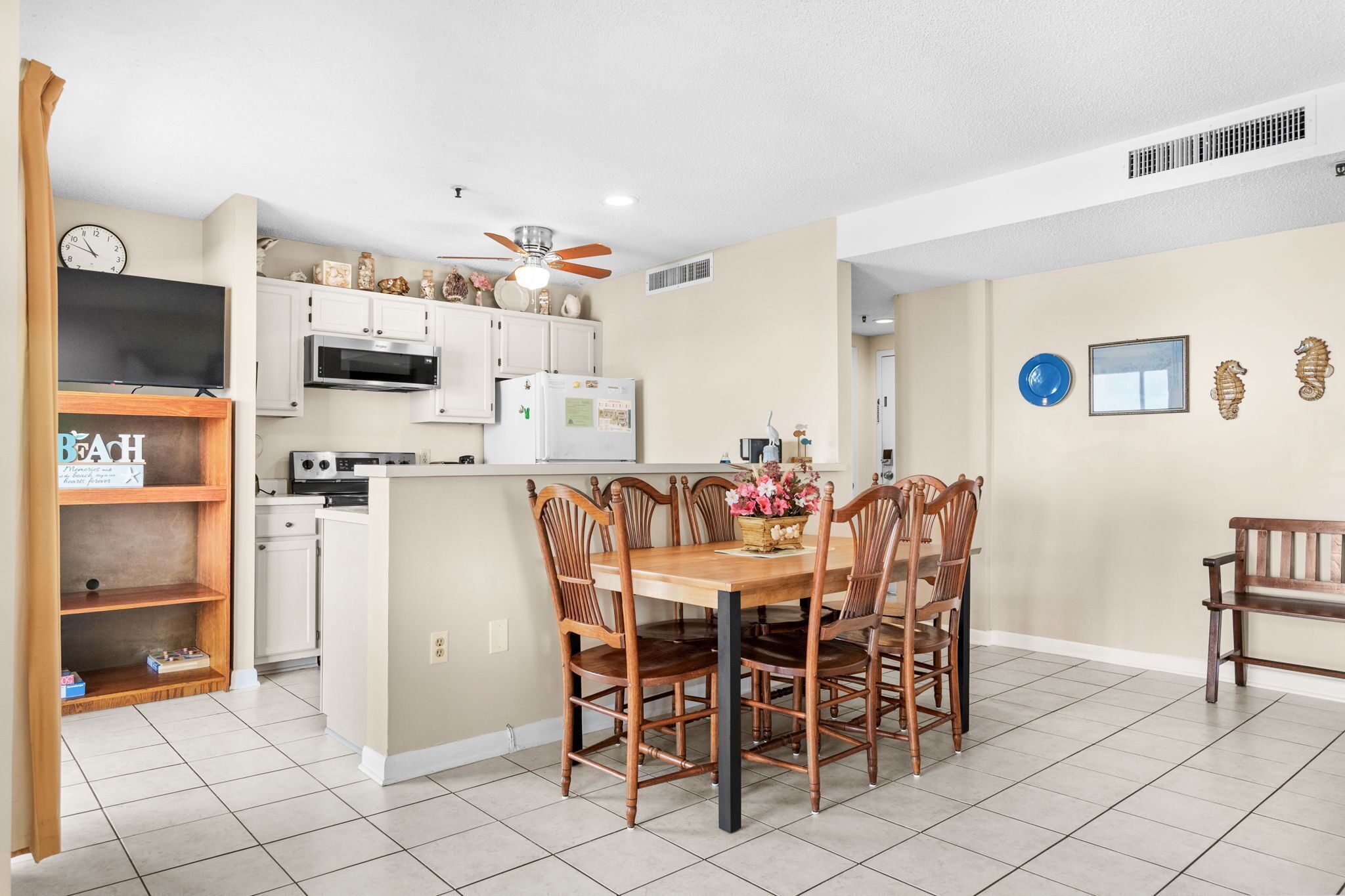 A compact kitchen with white cabinets, a microwave, and a refrigerator. There is a dining table with chairs and a bench.
