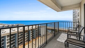 Een balkon met uitzicht op zee en strand, met een zithoek met stoelen en een vloerkleed.