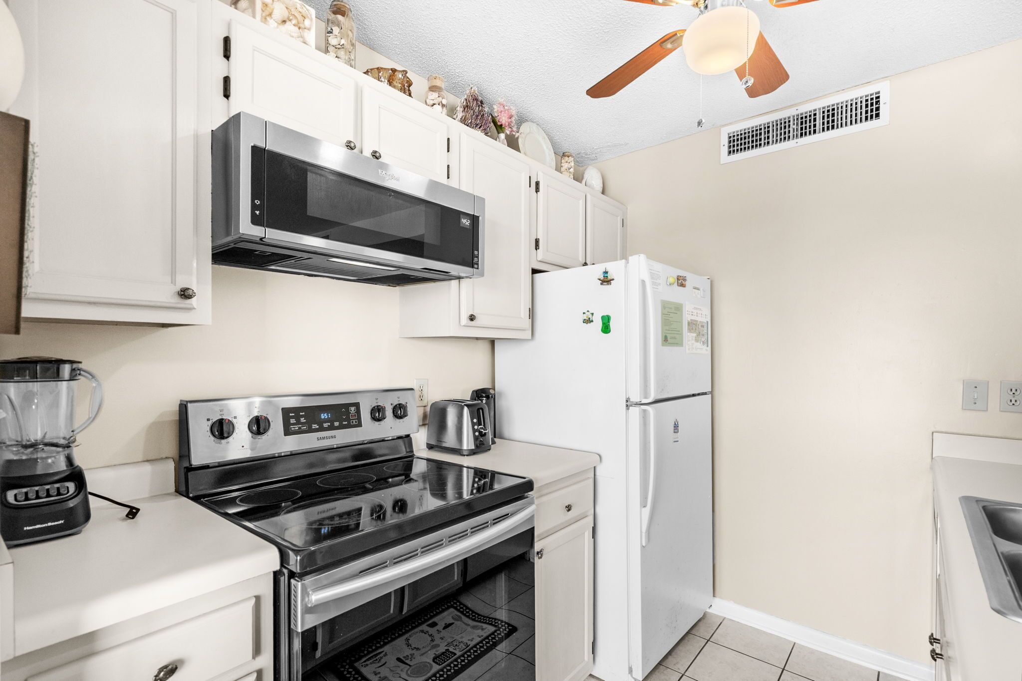A compact kitchen with white cabinets, a stainless steel stove, a microwave, and a refrigerator.
