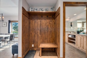 Un banc en bois dans un coin, un mur en bois avec une pancarte indiquant « À LOUER », un coin repas avec une table et des chaises, et une salle de bain avec un lavabo et un miroir.