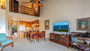 A spacious living area with a dining table, chairs, a sofa, a TV, and a bookshelf.