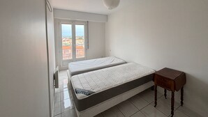 A bedroom with a bed, a wooden nightstand, and a window with a view of buildings. - Apartment with canal view, garage and wifi (Les Sables-d'Olonne)