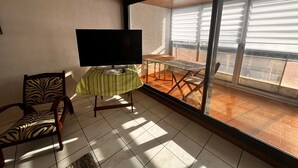 A balcony with a table and chairs, a television on a stand, and a zebra-patterned chair. - Apartment with canal view, garage and wifi (Les Sables-d'Olonne)