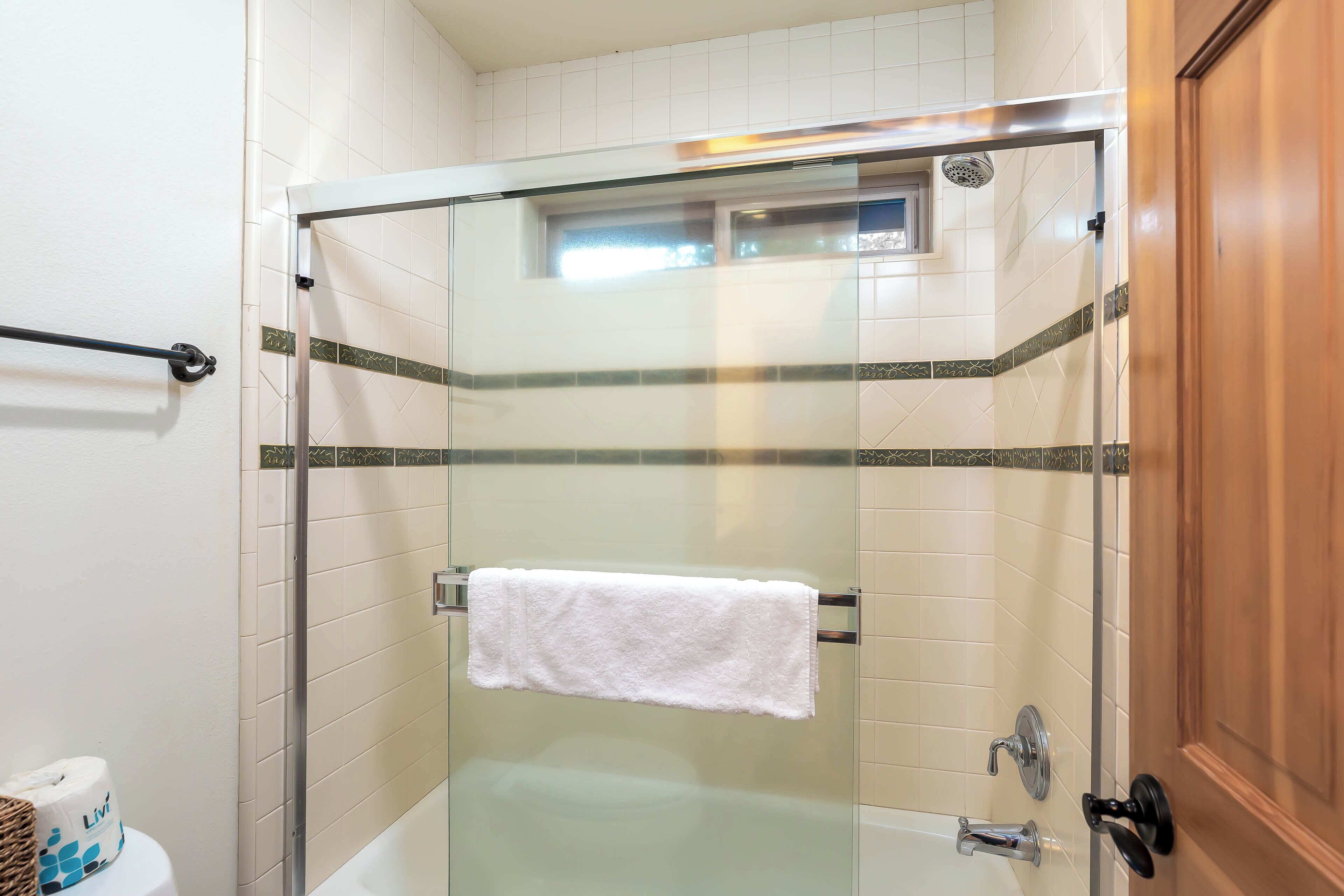 A glass-enclosed shower with a white towel hanging on a metal bar, beige tiled walls, and a wooden door.