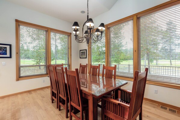 A dining area with a wooden table and chairs, large windows with blinds, and a chandelier. - Spacious 5BR for 12: Hot Tub, A/C, Foosball + Ping Pong, North Sunriver-BIGL18 (Sunriver)