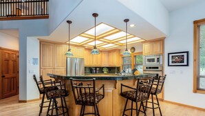 A modern kitchen with a central island, bar stools, and pendant lighting. - Spacious 5BR for 12: Hot Tub, A/C, Foosball + Ping Pong, North Sunriver-BIGL18 (Sunriver)