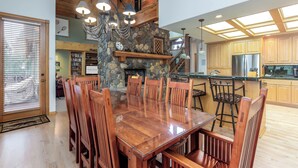 A spacious dining area with a large wooden table and chairs, a stone fireplace, and a kitchen with wooden cabinets and stainless steel appliances. - Spacious 5BR for 12: Hot Tub, A/C, Foosball + Ping Pong, North Sunriver-BIGL18 (Sunriver)