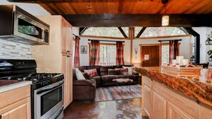 A kitchen with a stove, oven, and microwave, a wooden dining area with a bar, and a living room with a sofa and curtains.