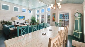 A dining area with a wooden table, teal chairs, a green clock, and a view of buildings through large windows. - Come and play at our Blue Hawaiian Beach house! Close to the beach! The perfect (Port Aransas)