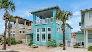 A two-story building with a balcony, surrounded by palm trees and a white picket fence. - Come and play at our Blue Hawaiian Beach house! Close to the beach! The perfect (Port Aransas)