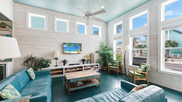 A spacious living room with a blue leather sofa, a wooden coffee table, and a television mounted on the wall. - Come and play at our Blue Hawaiian Beach house! Close to the beach! The perfect (Port Aransas)