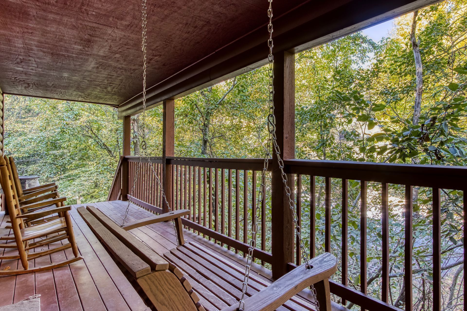 Una terraza de madera con un columpio y un banco, rodeada de árboles.
