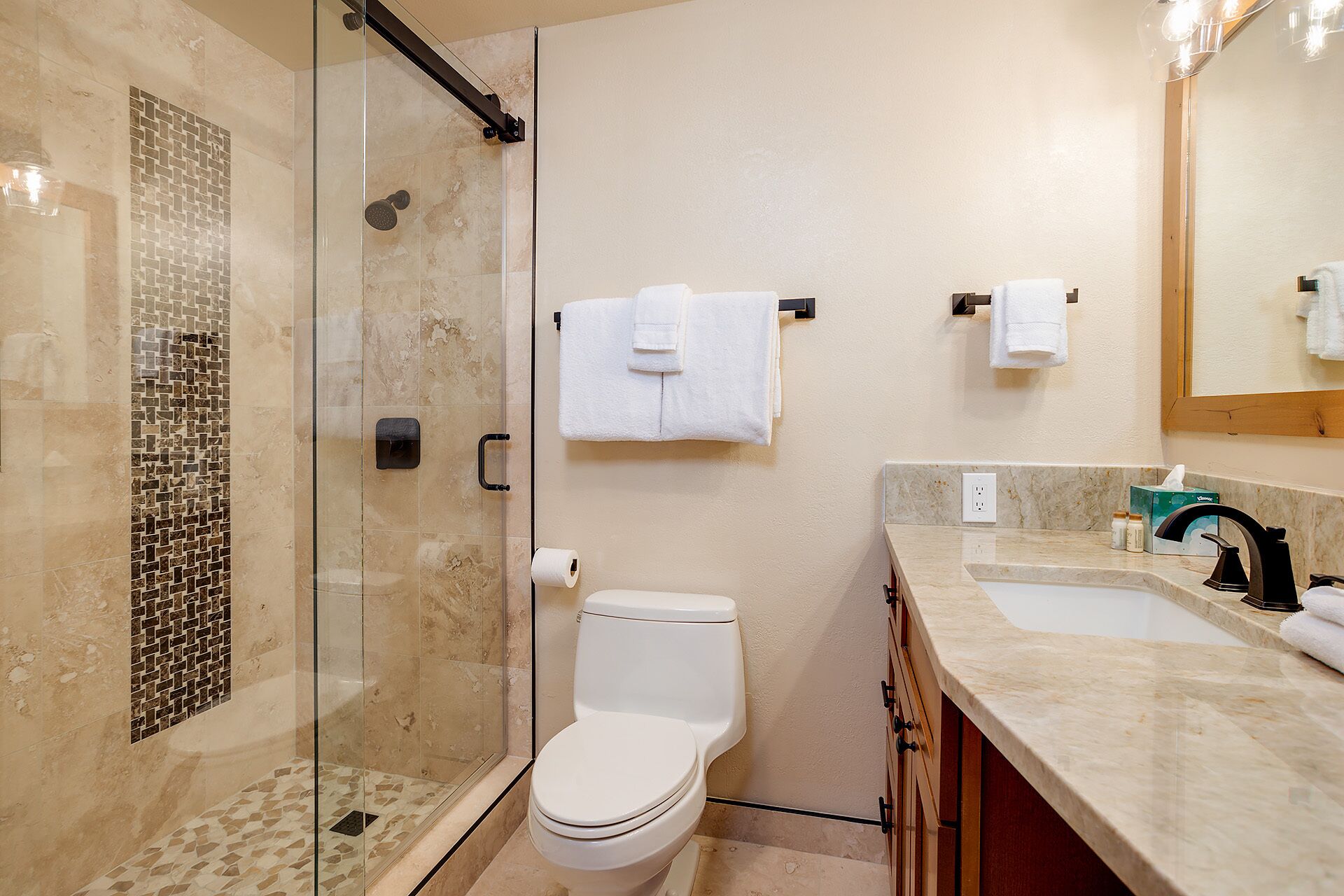 Un baño moderno con ducha envuelta en vidrio, inodoro y tocador con lavamanos y espejo.