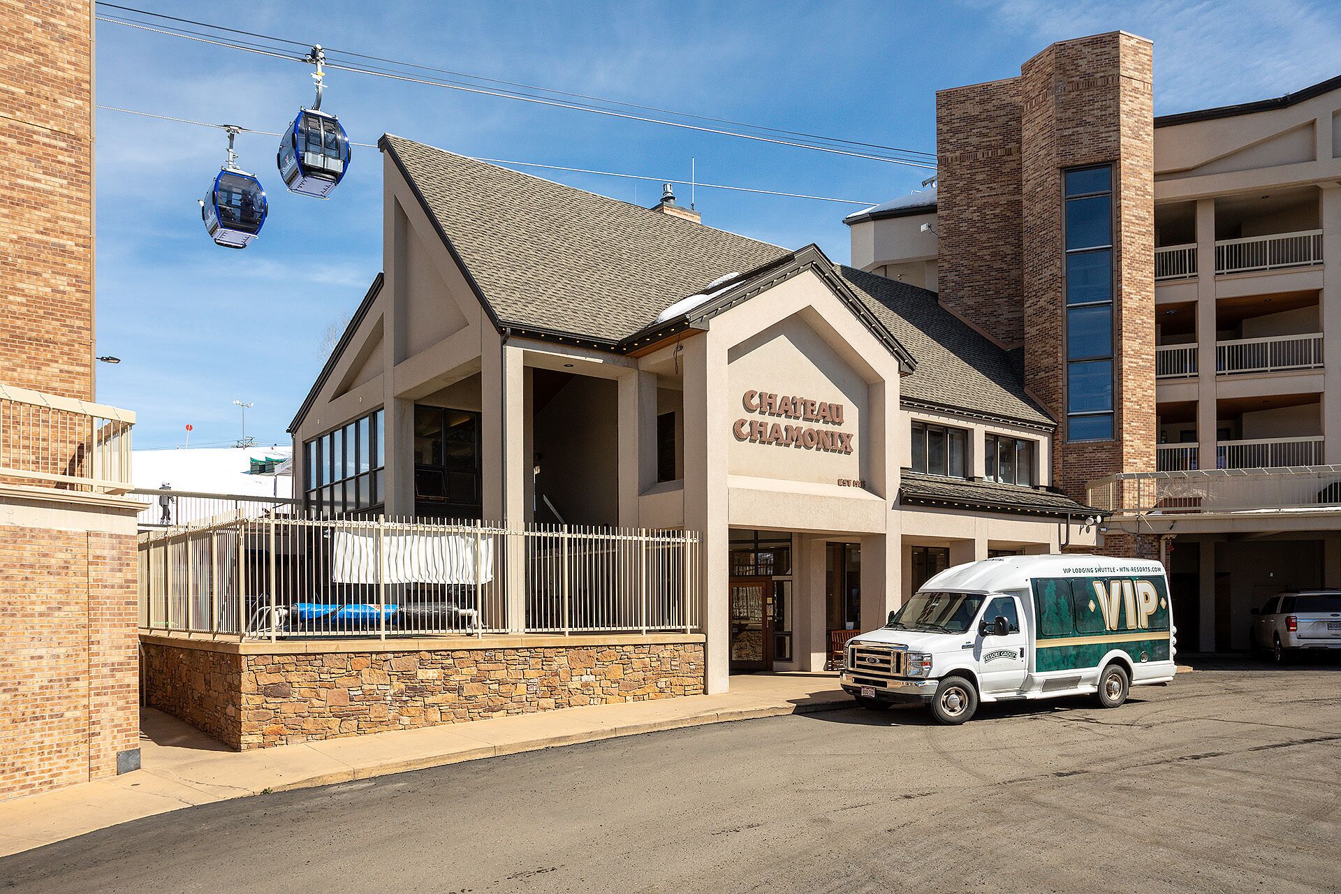 Um hotel com uma placa indicando 'CHATEAU CHAMONIX', fachada de pedra e área de estacionamento com van de serviço de transporte.