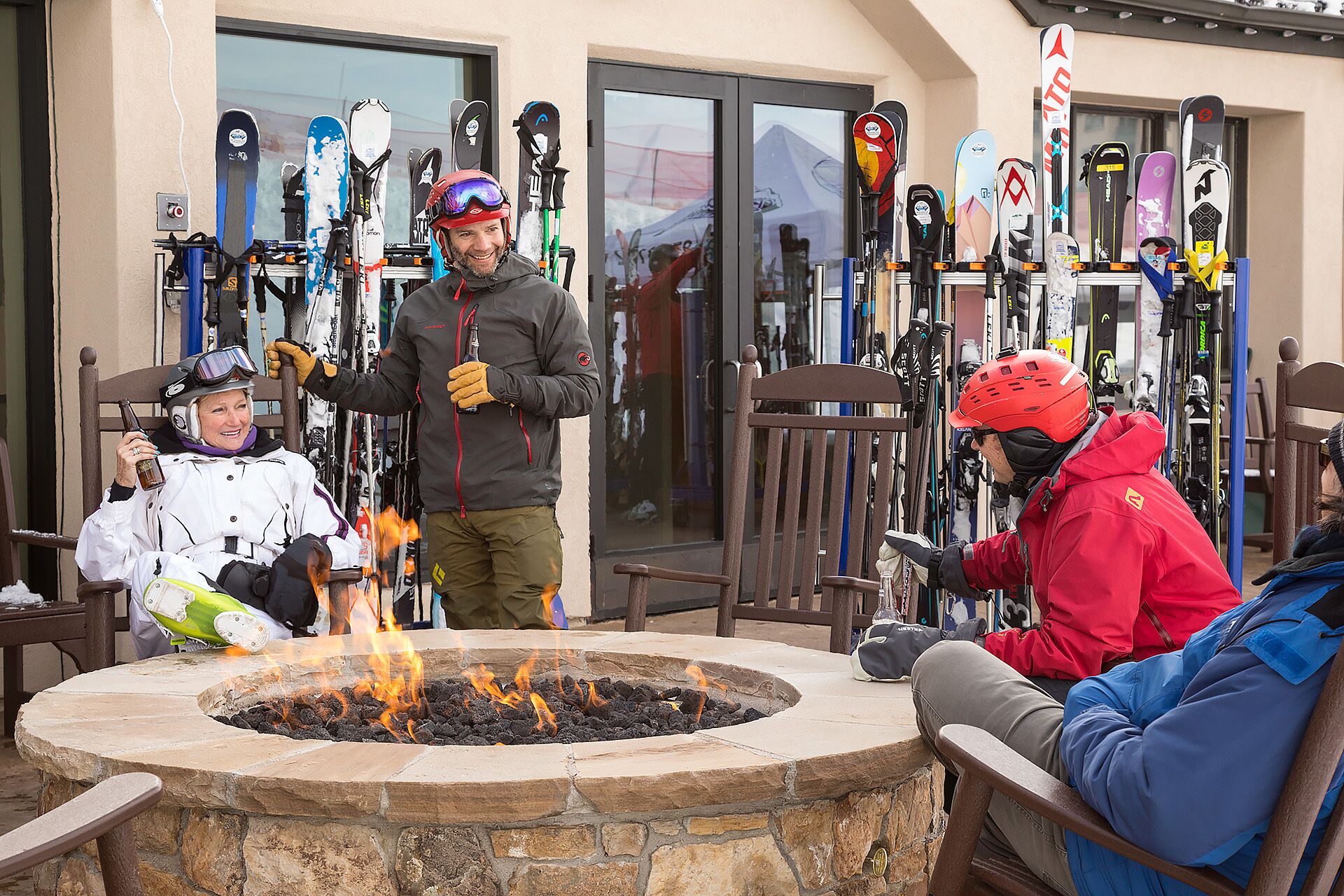 A stone fire pit with flames, surrounded by chairs and people.