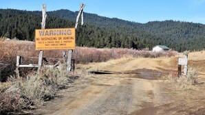 A warning sign on a rural road with a forested mountain in the background.