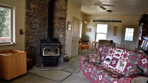 A cozy living room with a stone fireplace, a wooden chest, and a plaid-patterned sofa.