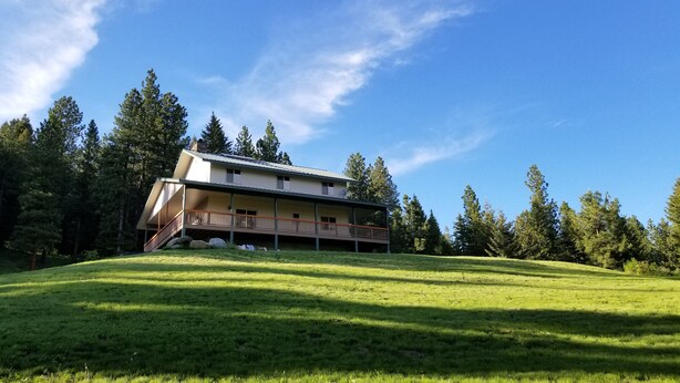 A two-story building with a balcony on the upper floor, surrounded by a grassy area and trees.