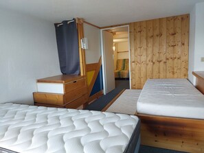 Quarto com duas camas, uma cômoda de madeira, uma cortina e uma parede de madeira.