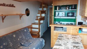 A compact kitchen with a microwave, oven, and sink, a wooden staircase, and a blue sofa with floral upholstery. - Comfortable duplex for 6 people in Arc 1800 (Les Arcs 1800)