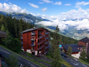 Un edificio de madera de varios pisos con balcones, rodeado de vegetación exuberante y montañas al fondo.