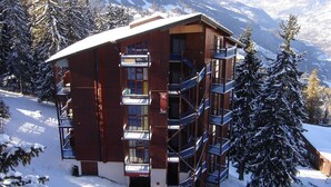 A wooden chalet with multiple balconies, surrounded by snow-covered trees and mountains. - Comfortable duplex for 6 people in Arc 1800 (Les Arcs 1800)
