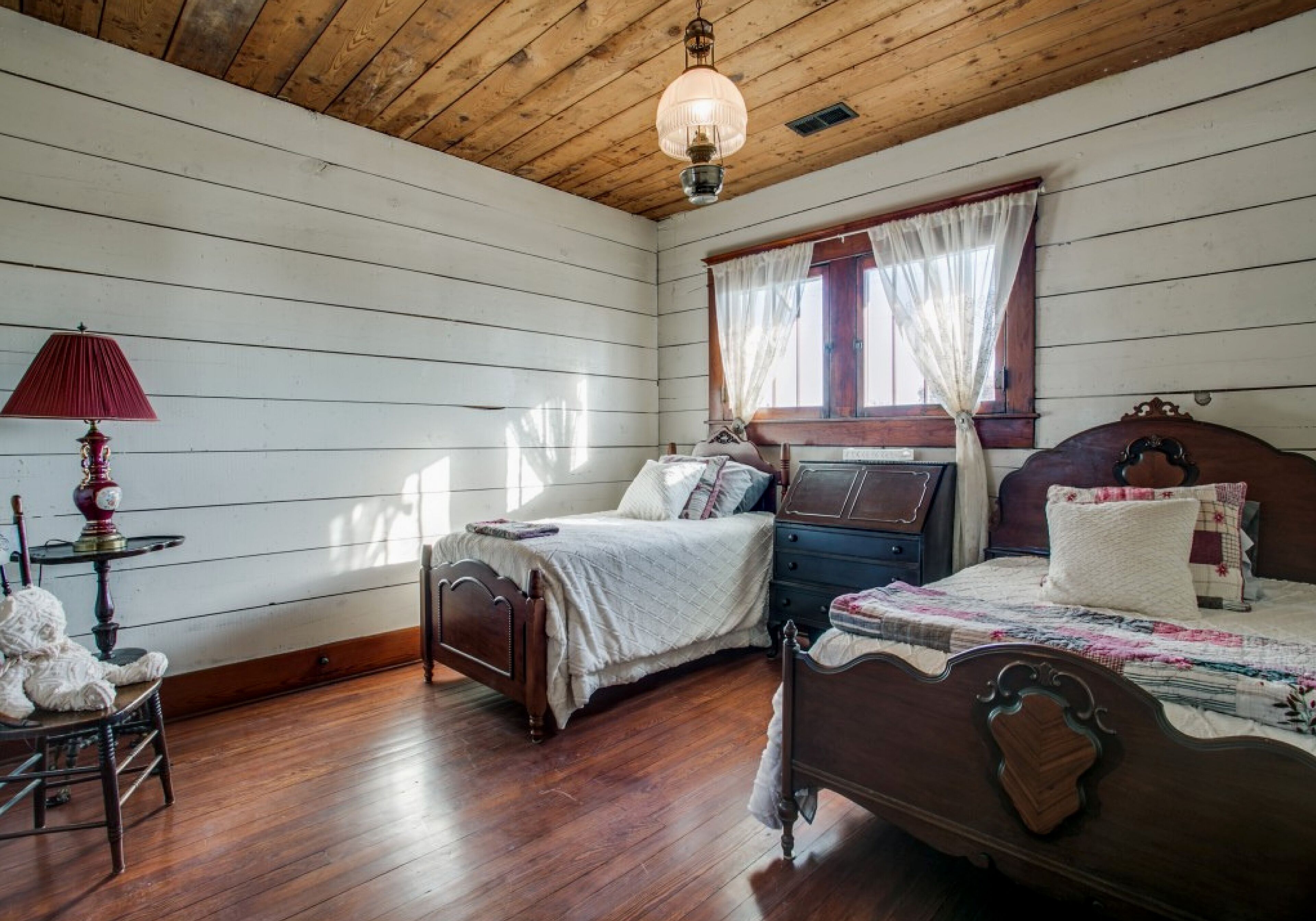 A bedroom with two wooden beds, a red lamp, and a teddy bear on a chair.