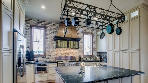 A kitchen with a large island, white cabinetry, a brick wall, and hanging pots. - Gorgeous 20s Historic Mini Mansion. King & Queens. Downtown Strip. (Wylie)