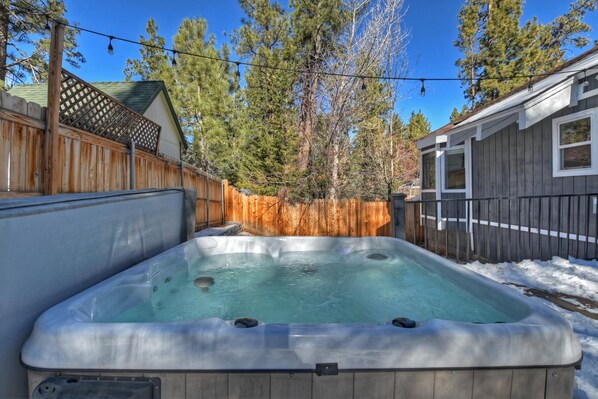 A hot tub in a backyard with a wooden fence, a shed, and trees.