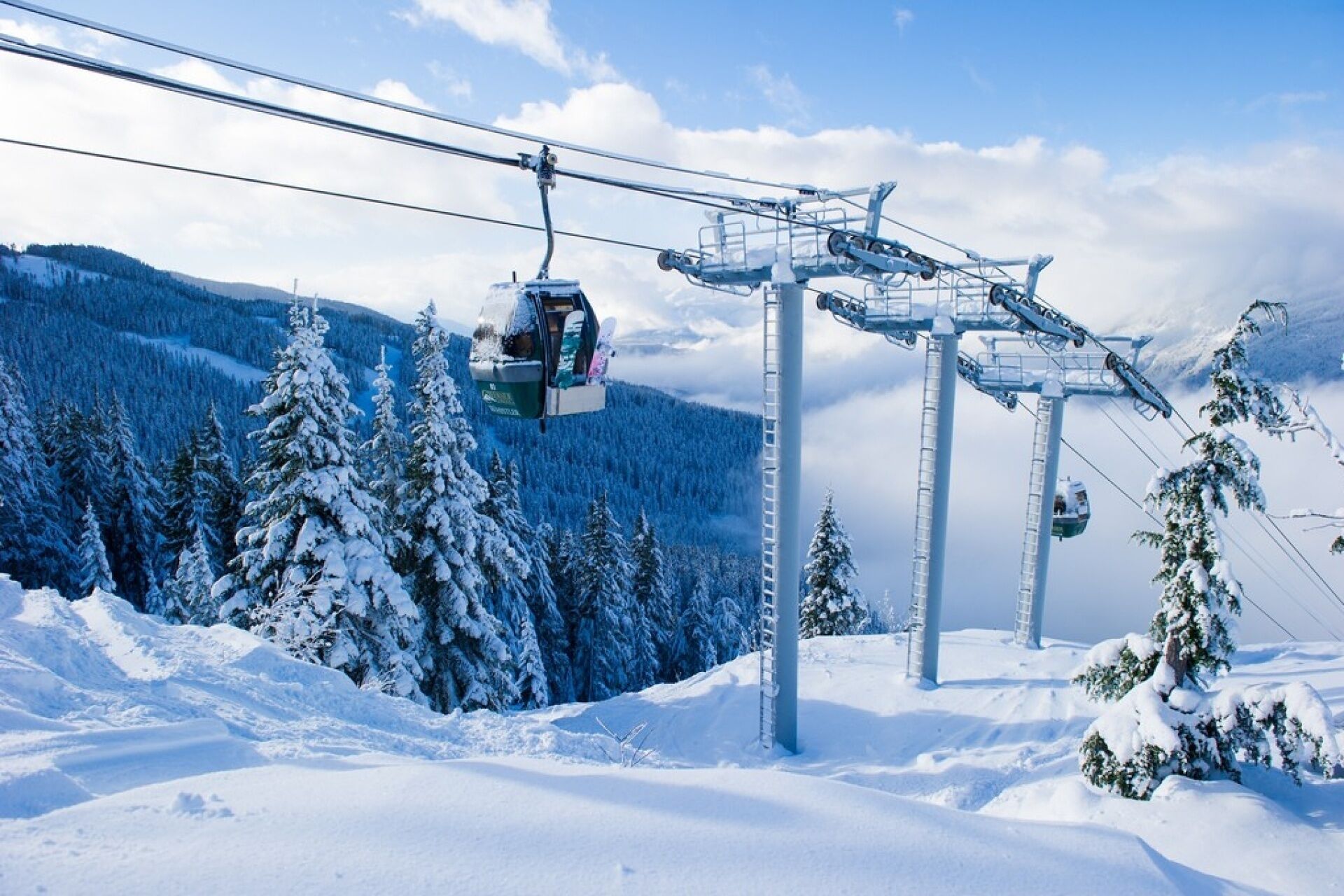 A cable car system in a snowy mountainous area with trees and a clear sky.