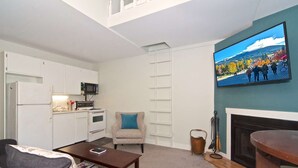 A compact living space with a kitchenette, a sofa, a coffee table, a fireplace, and a television mounted on the wall. - Cute and Cozy Creekside townhouse. Ground floor, easy access, free parking, 100 meters to lifts (Whistler)