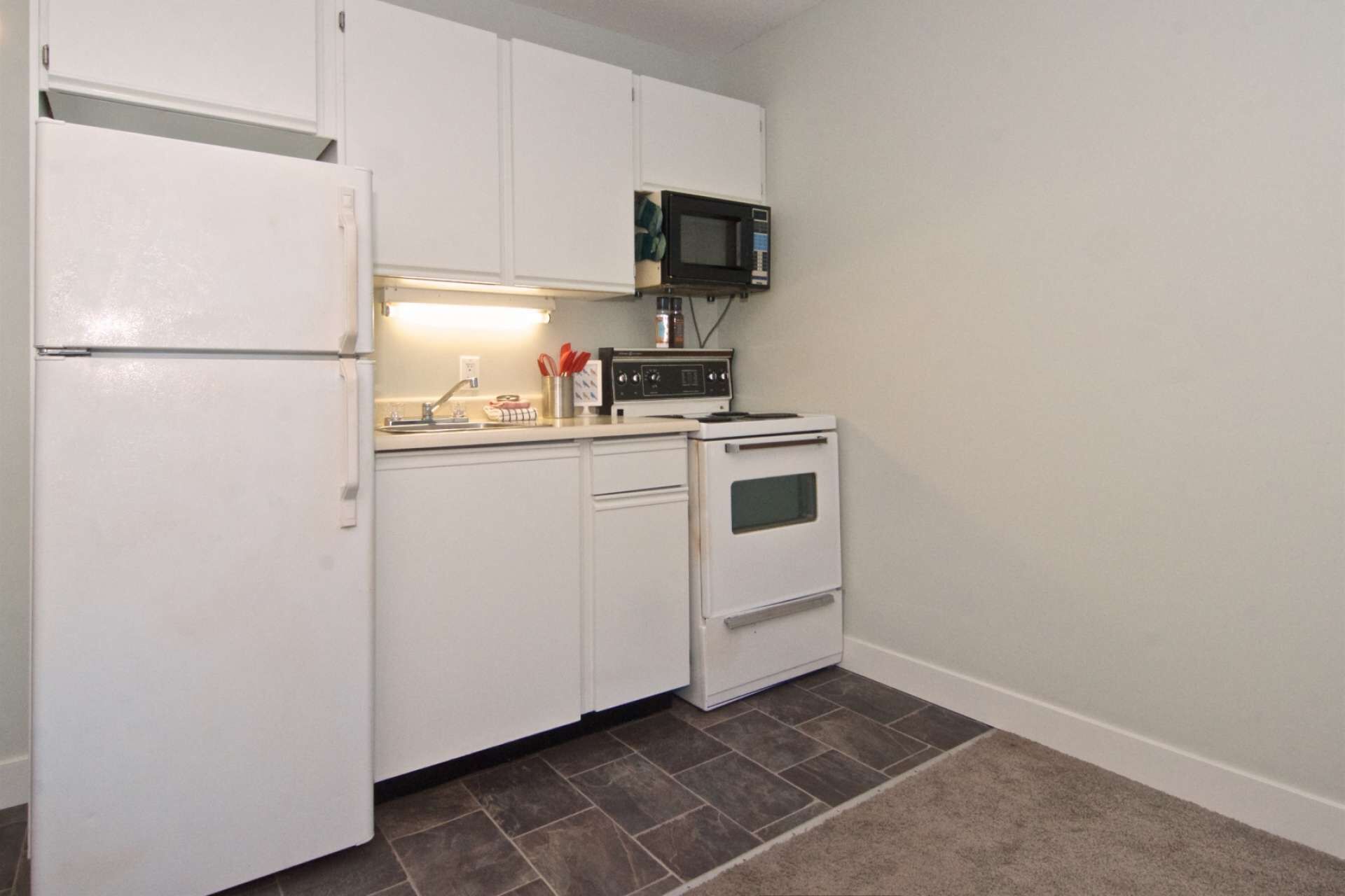 A compact kitchen with white cabinets, a microwave, a stove, and a refrigerator.