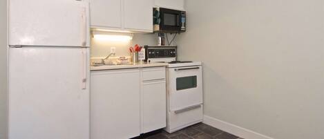 A compact kitchen with white cabinets, a microwave, a stove, and a refrigerator.
