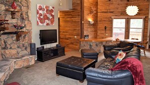 Ein gemütliches Wohnzimmer mit Kamin aus Stein, einem Flachbildfernseher, Ledersofas und einem Essbereich aus Holz.