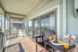 A wooden deck with a table set for breakfast, including a plate of fruit, a pitcher of orange juice, and a vase of flowers.