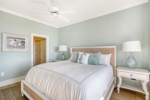 A bedroom with a large bed, two bedside tables with lamps, a ceiling fan, and a framed picture on the wall.