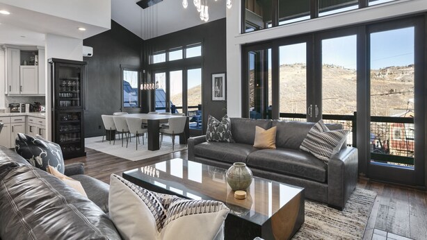A modern living room with a large sofa, a coffee table, and a dining area with a kitchen in the background. - Ski-In/Ski-Out Home, Private Hot Tub (Park City)