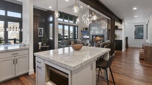 A modern kitchen with a large island, pendant lights, and a fireplace. - Ski-In/Ski-Out Home, Private Hot Tub (Park City)