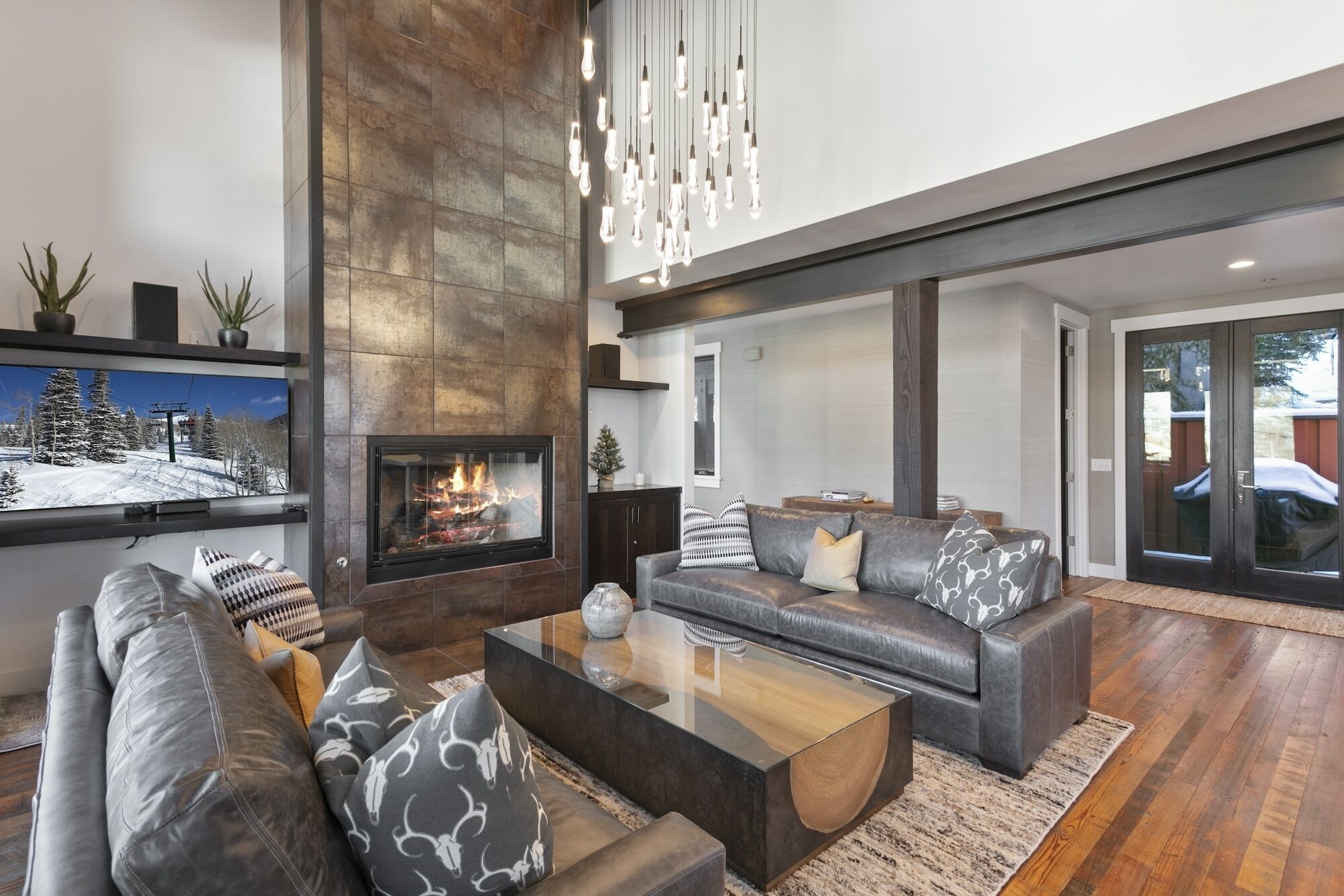 A modern living room with a fireplace, leather sofas, a coffee table, and a large TV screen displaying a snowy landscape.