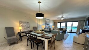 A spacious living area with a dining table, chairs, sofas, and a balcony with a view.