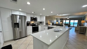 A modern kitchen with stainless steel appliances, a large island, and a view to the living area.