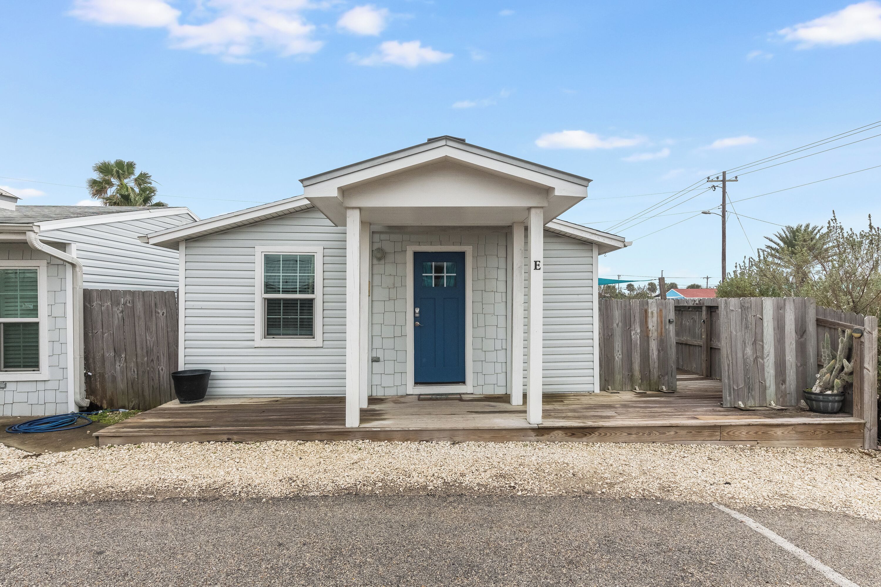 Ein eingeschossiges Haus mit einer blauen Haustür, einer Veranda und einem Holzzaun.