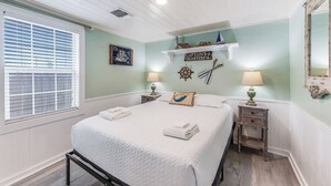 Une chambre à coucher comprenant un lit, deux tables de chevet, une fenêtre avec des stores, une étagère murale agrémentée d’objets décoratifs et un miroir.